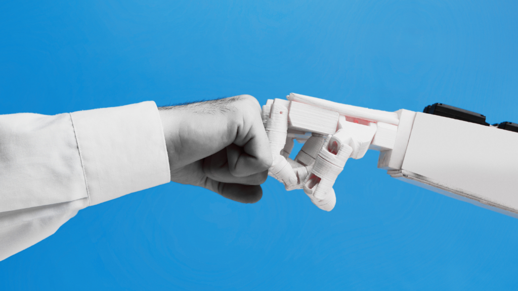 The image shows a close-up of a human fist bumping with a robotic hand against a solid blue background. The human hand is wearing a white long-sleeve shirt, while the robotic hand is white with visible mechanical joints and wires. The image represents the interaction and collaboration between humans and robots or artificial intelligence.